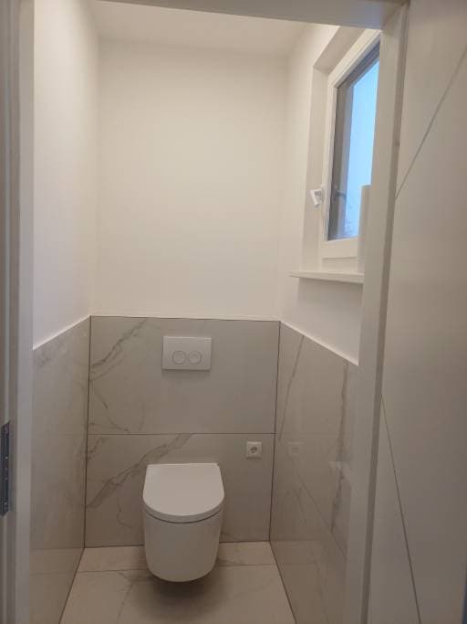 Fertiggestelltes WC mit hängendem Wandtiefspüler und Marmoroptik-Fliesen