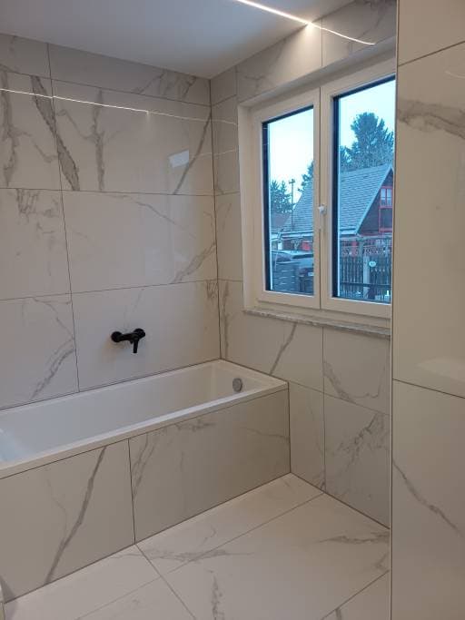 Fertiggestelltes Badezimmer mit Badewanne, schwarzen Armaturen und Marmoroptik-Fliesen