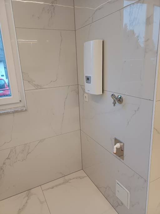 Fertiggestelltes Badezimmer mit Warmwasserboiler und Marmoroptik-Fliesen